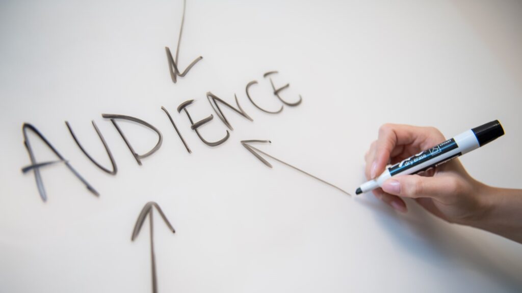 A person using a black marker to draw arrows to the word "audience" on a whiteboard.
